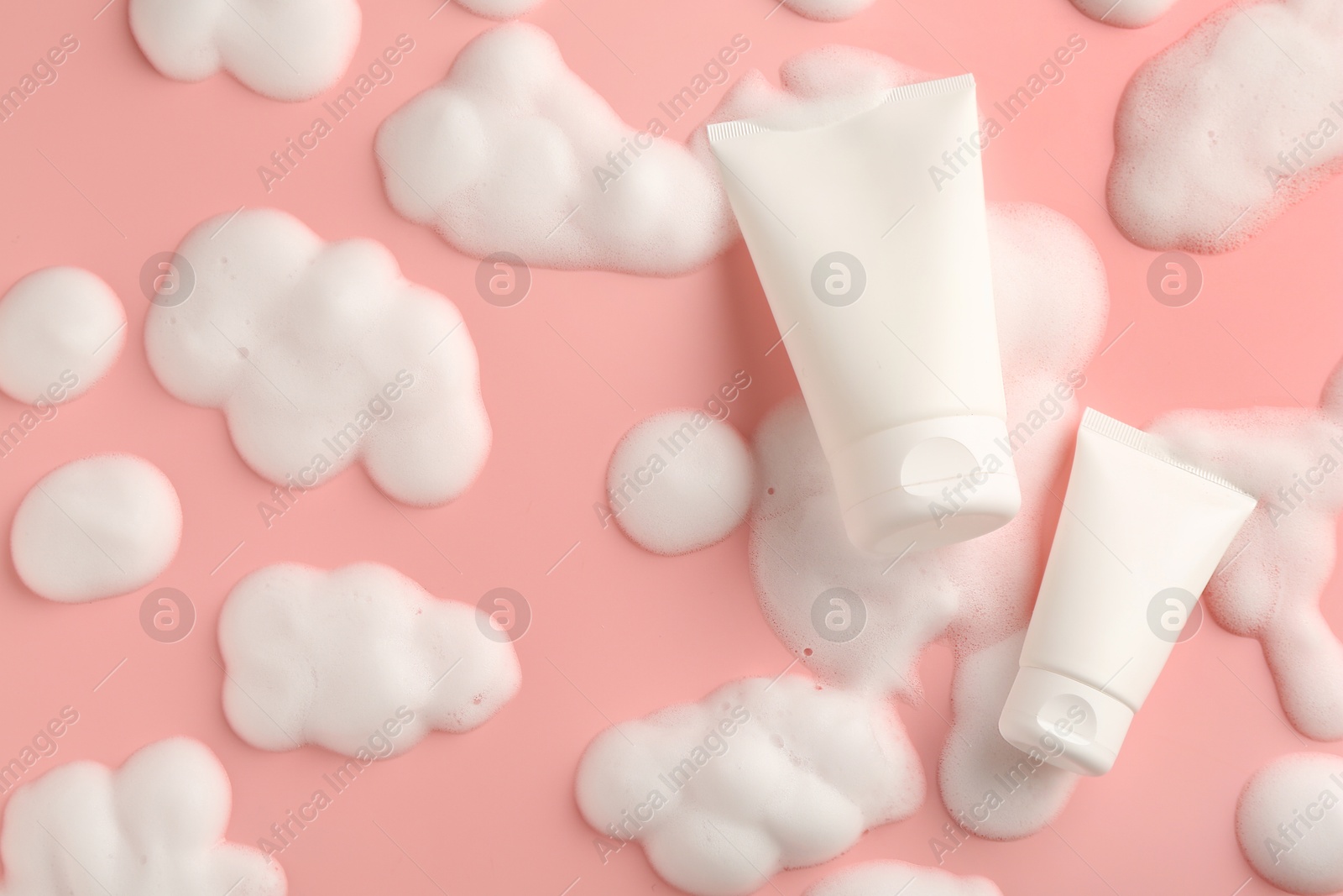 Photo of Tubes of cosmetic products with foam on pink background, top view. Space for text