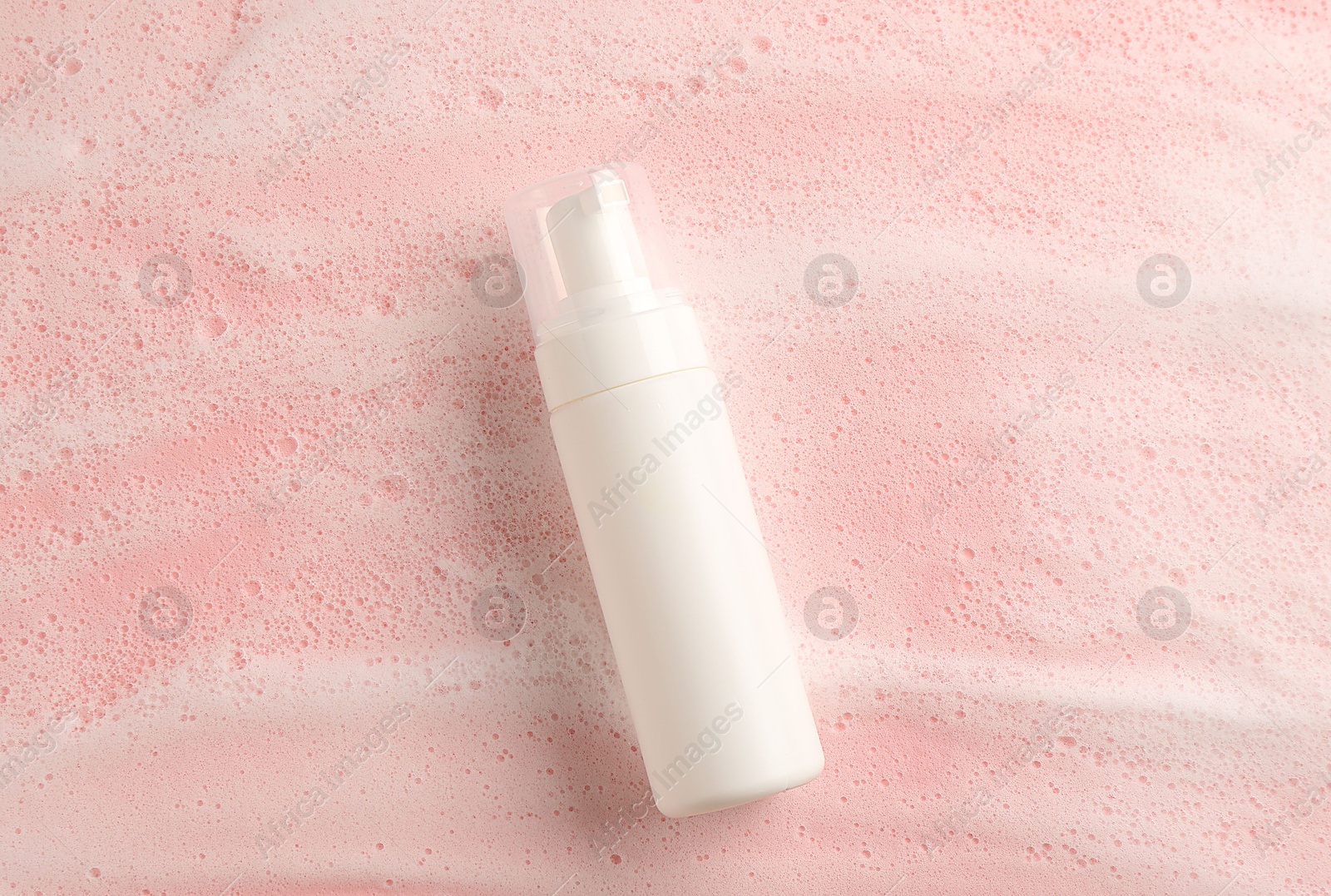 Photo of Bottle of cosmetic product with foam on pink background, top view