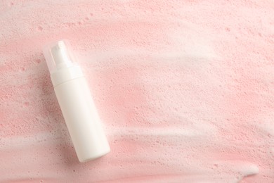 Photo of Bottle of cosmetic product with foam on pink background, top view. Space for text