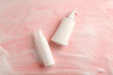 Photo of Bottles of cosmetic products with foam on pink background, top view