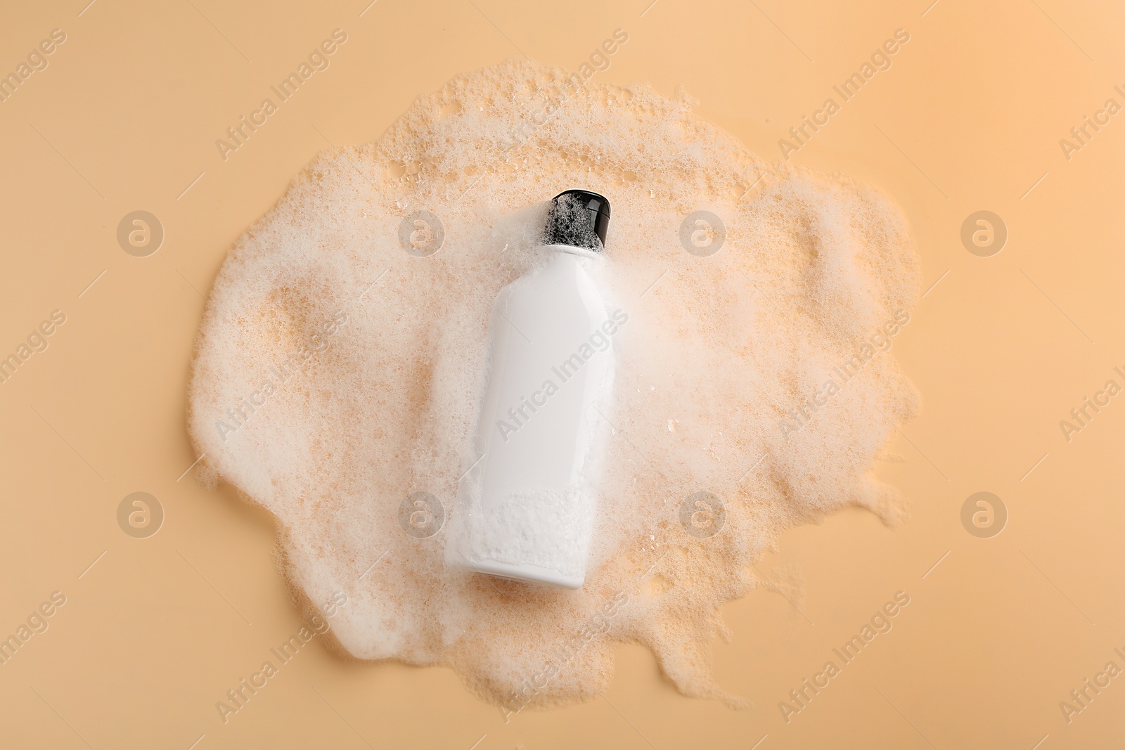 Photo of Bottle of cosmetic product with foam on beige background, top view