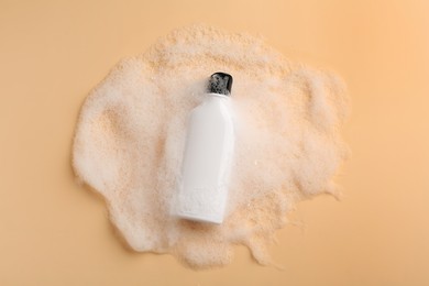 Bottle of cosmetic product with foam on beige background, top view