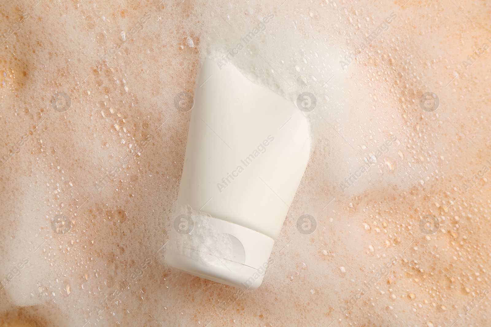 Photo of Tube of cosmetic product with foam on beige background, top view