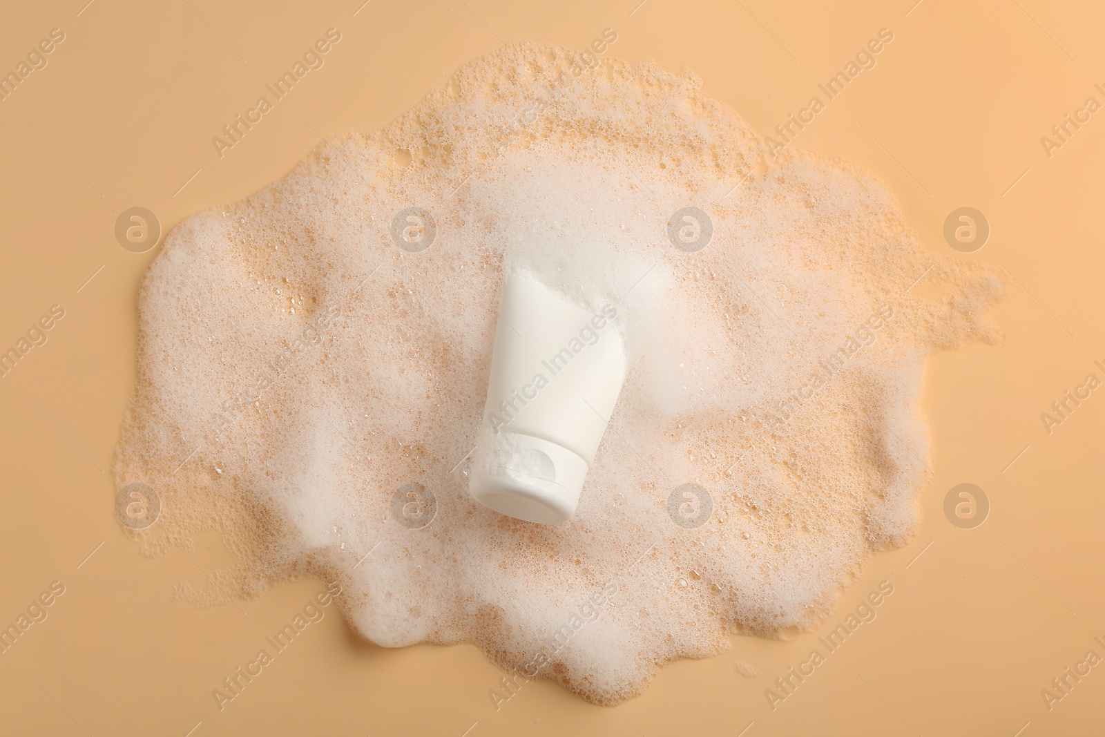 Photo of Tube of cosmetic product with foam on beige background, top view