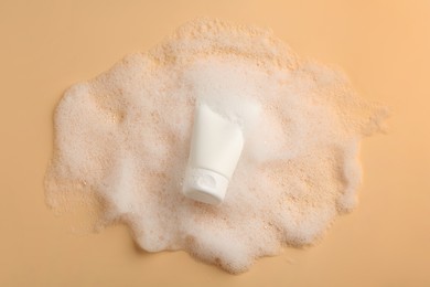 Photo of Tube of cosmetic product with foam on beige background, top view