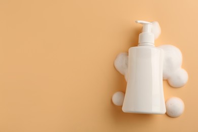 Photo of Bottle of cosmetic product with foam on beige background, top view. Space for text