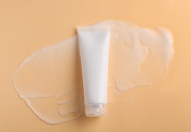 Photo of Tube of cosmetic product with foam on beige background, top view