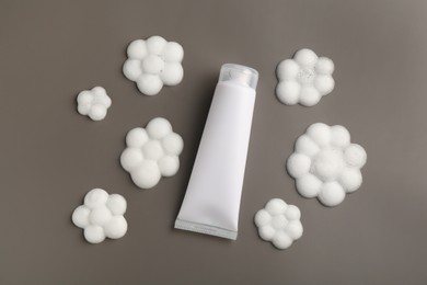 Photo of Tube of cosmetic product with foam in shape of flowers on grey background, top view