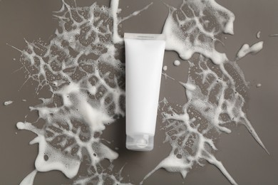 Tube of cosmetic product with foam on grey background, top view