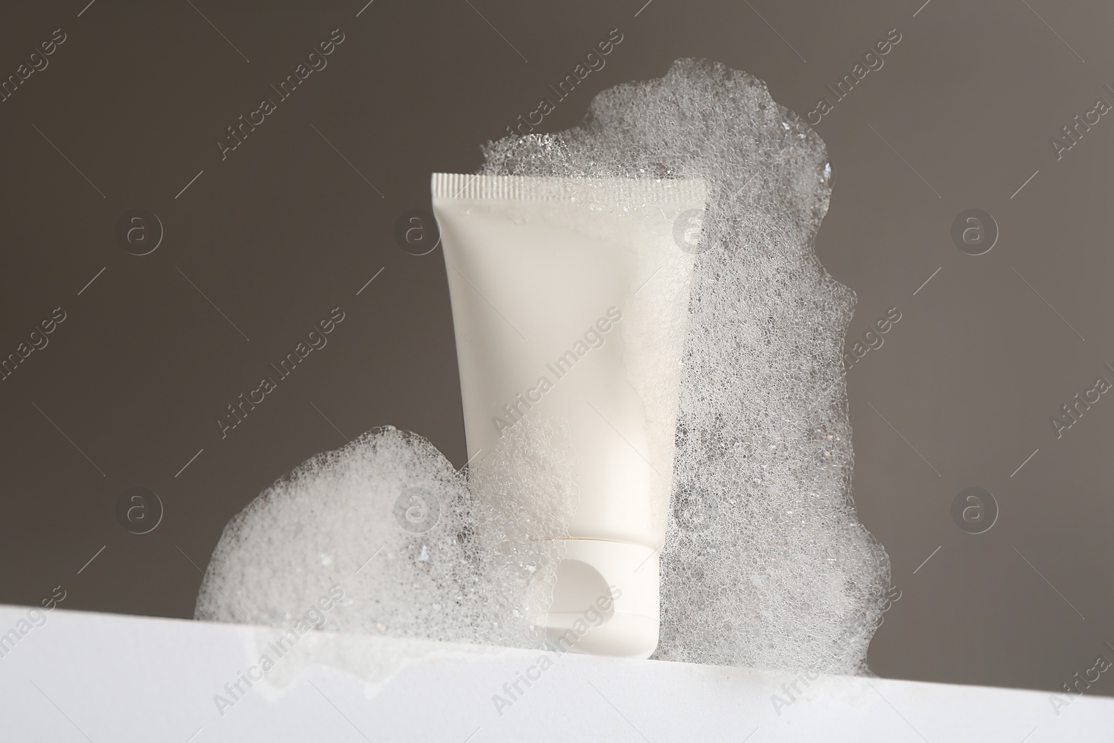 Photo of Tube of cosmetic product with foam on white surface against grey background