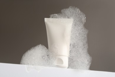 Tube of cosmetic product with foam on white surface against grey background