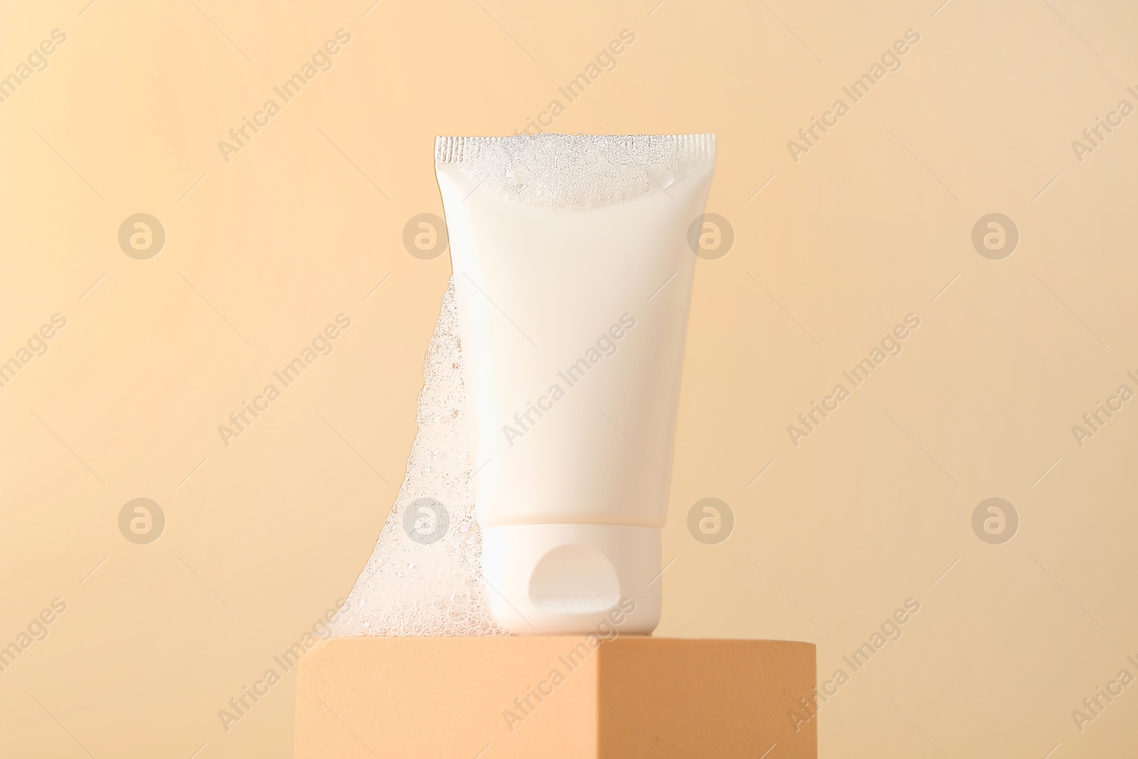 Photo of Tube of cosmetic product with foam on podium against beige background