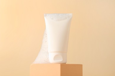 Tube of cosmetic product with foam on podium against beige background