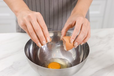 Photo of Making dough. Woman adding egg into bowl at white marble table, closeup