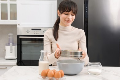 Photo of Making dough. Woman sifting flour into bowl at white table