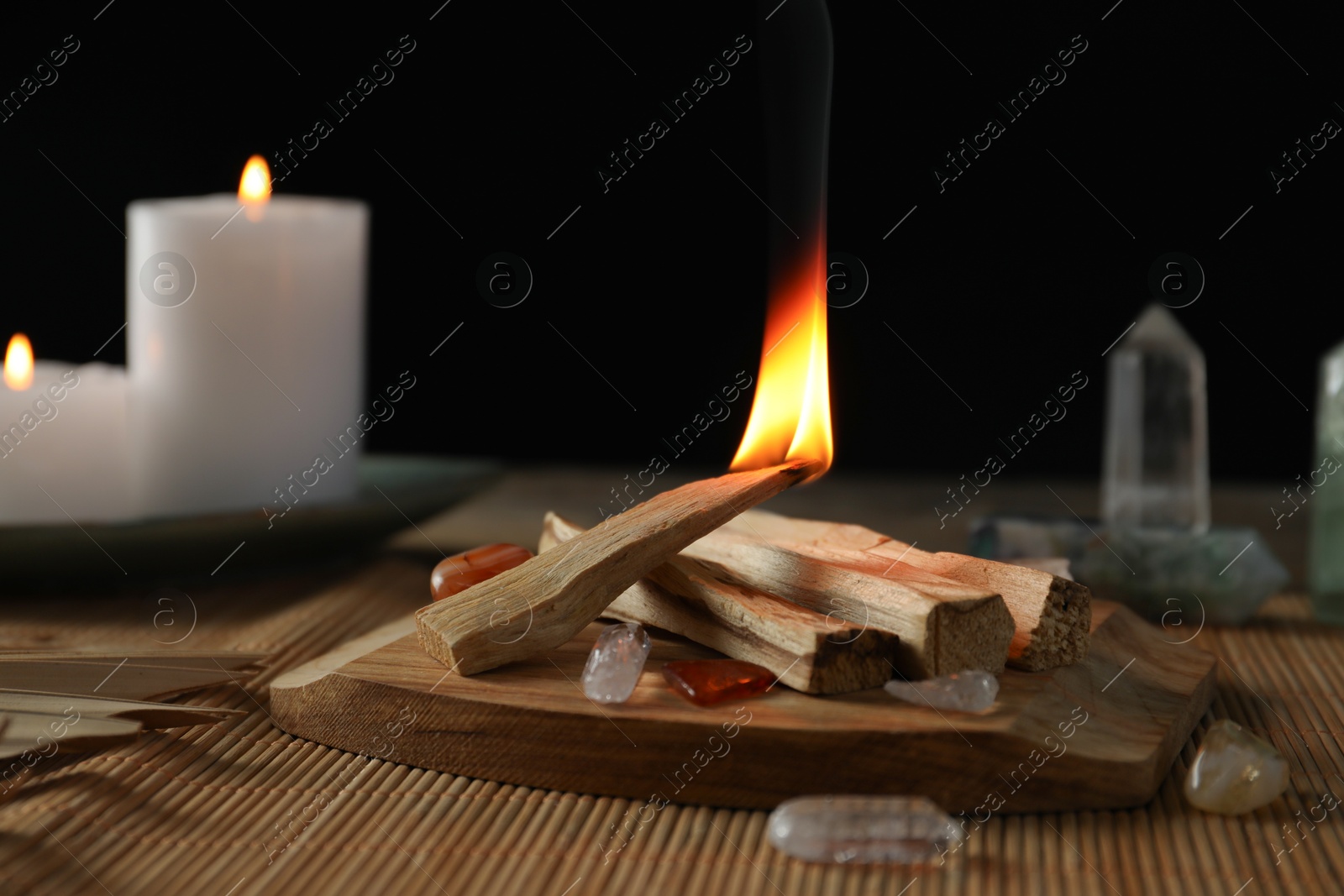 Photo of Burning palo santo stick, gemstones and candles on table, closeup