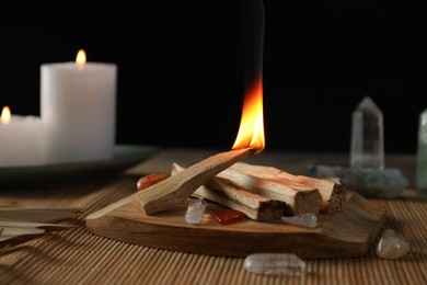 Photo of Burning palo santo stick, gemstones and candles on table, closeup