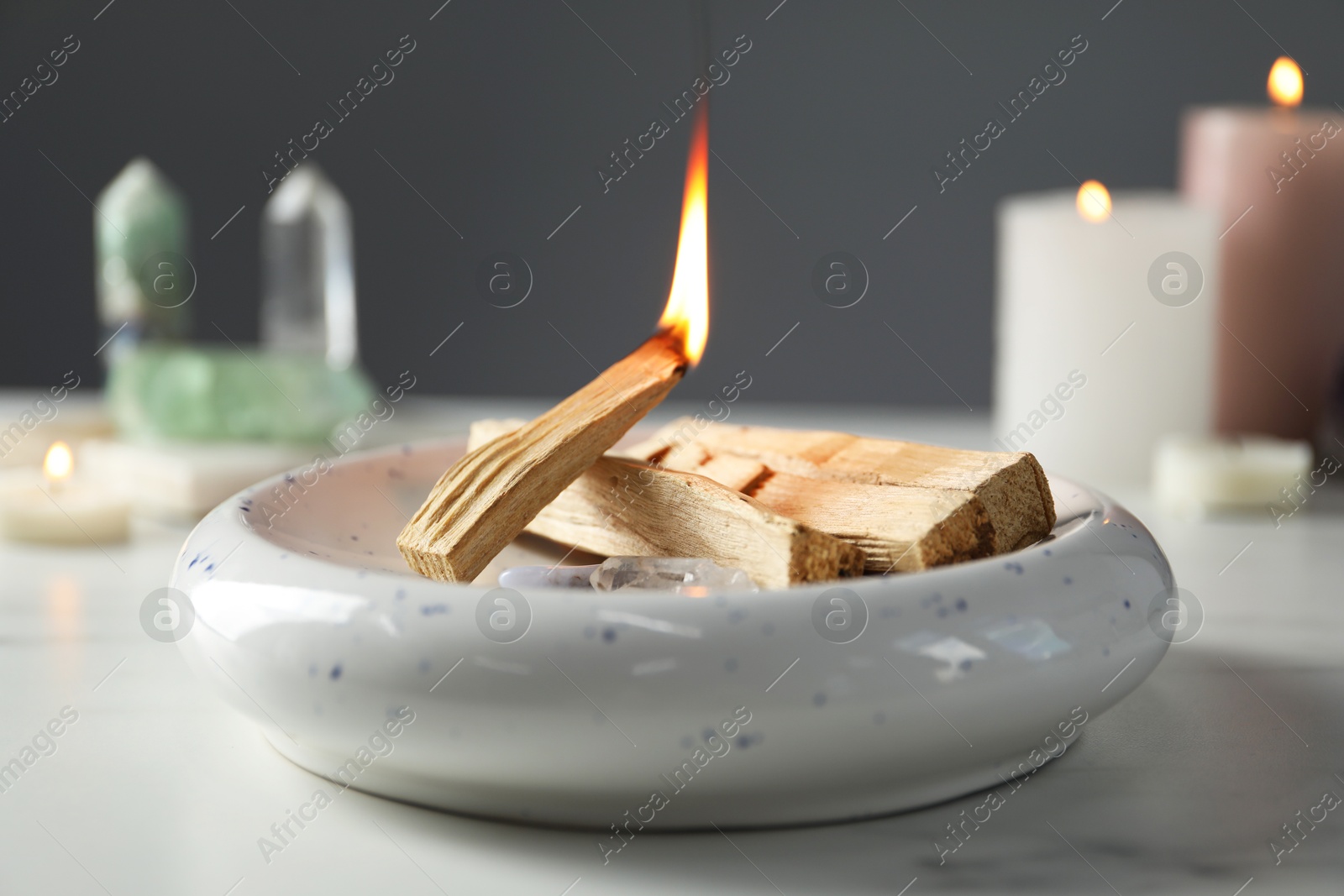 Photo of Burning palo santo stick and gemstones on white table, closeup