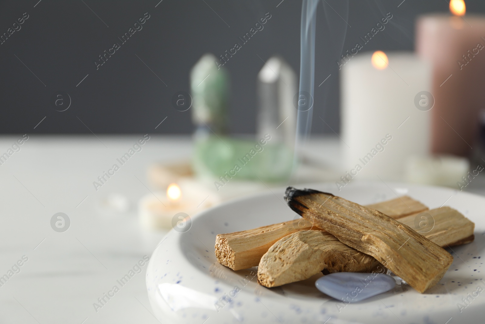 Photo of Smoldering palo santo stick and gemstone on table, closeup. Space for text