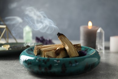 Photo of Smoldering palo santo stick and gemstone on grey table, closeup