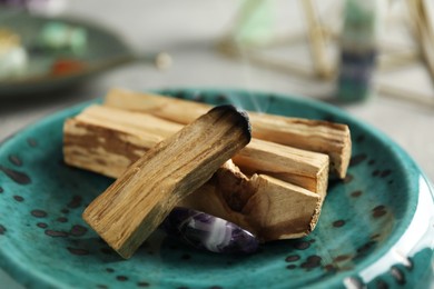 Photo of Smoldering palo santo stick and gemstone on table, closeup