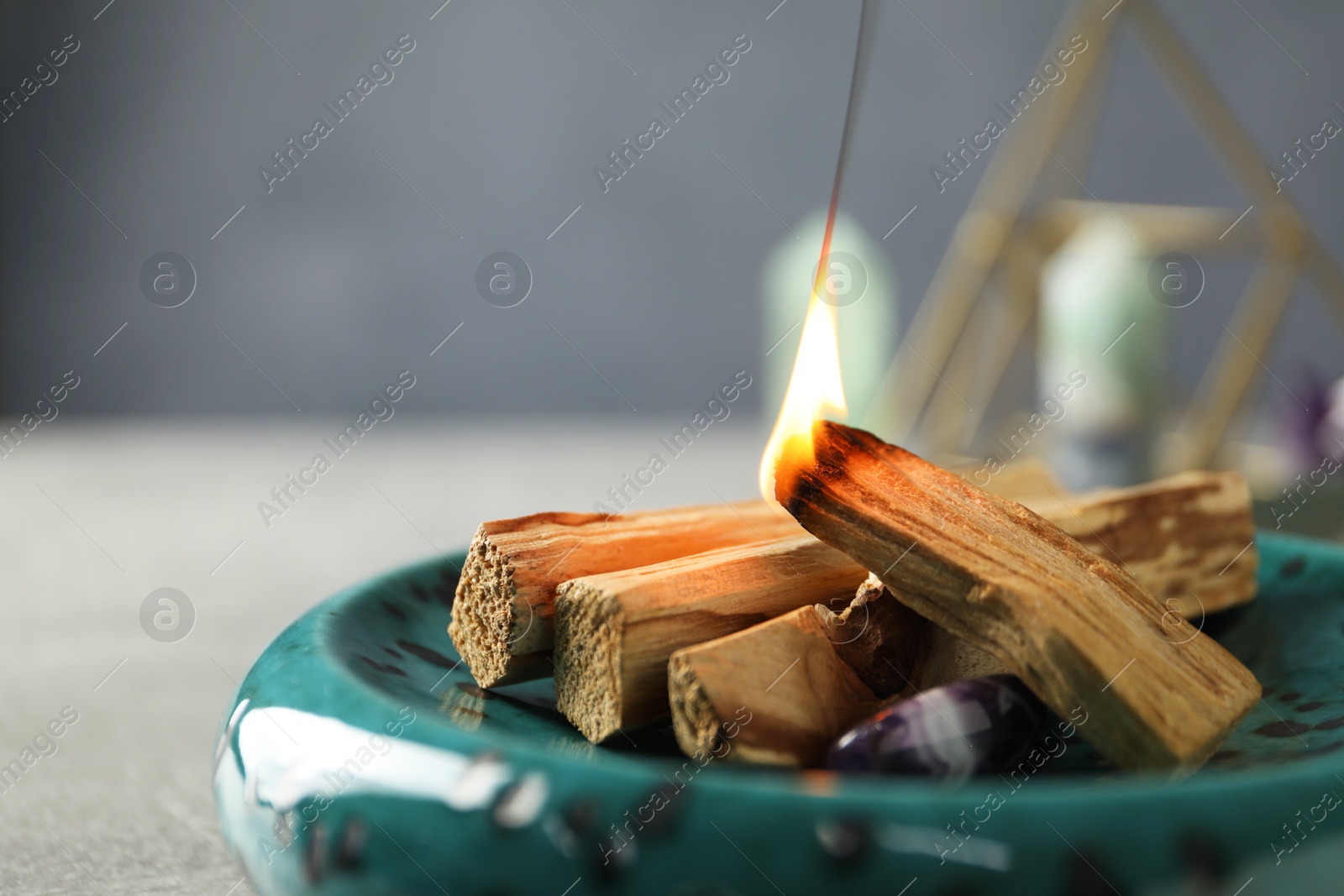 Photo of Burning palo santo stick and gemstone on table, closeup