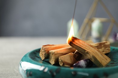 Photo of Burning palo santo stick and gemstone on table, closeup