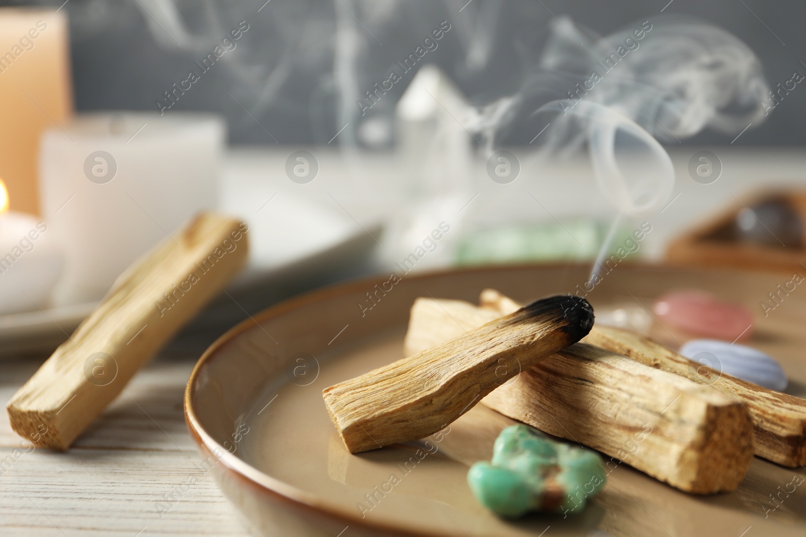 Photo of Smoldering palo santo stick and gemstones on wooden table, closeup