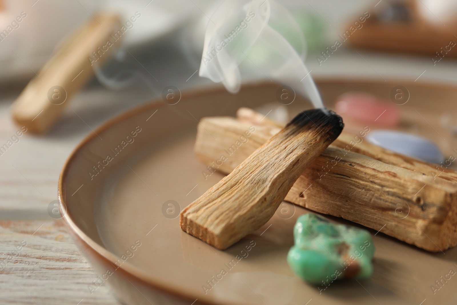 Photo of Smoldering palo santo stick and gemstones on wooden table, closeup