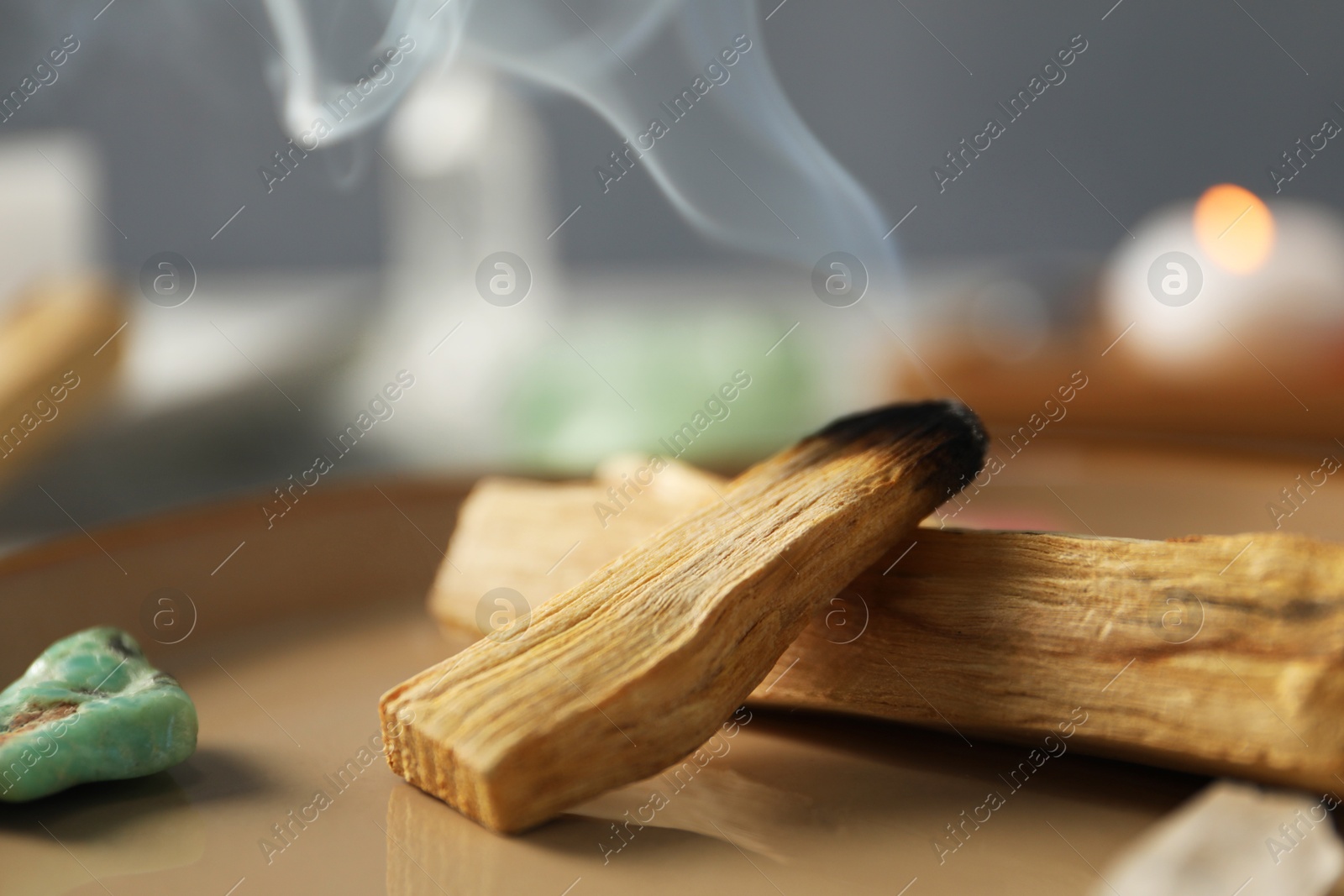 Photo of Smoldering palo santo stick and gemstones on plate, closeup