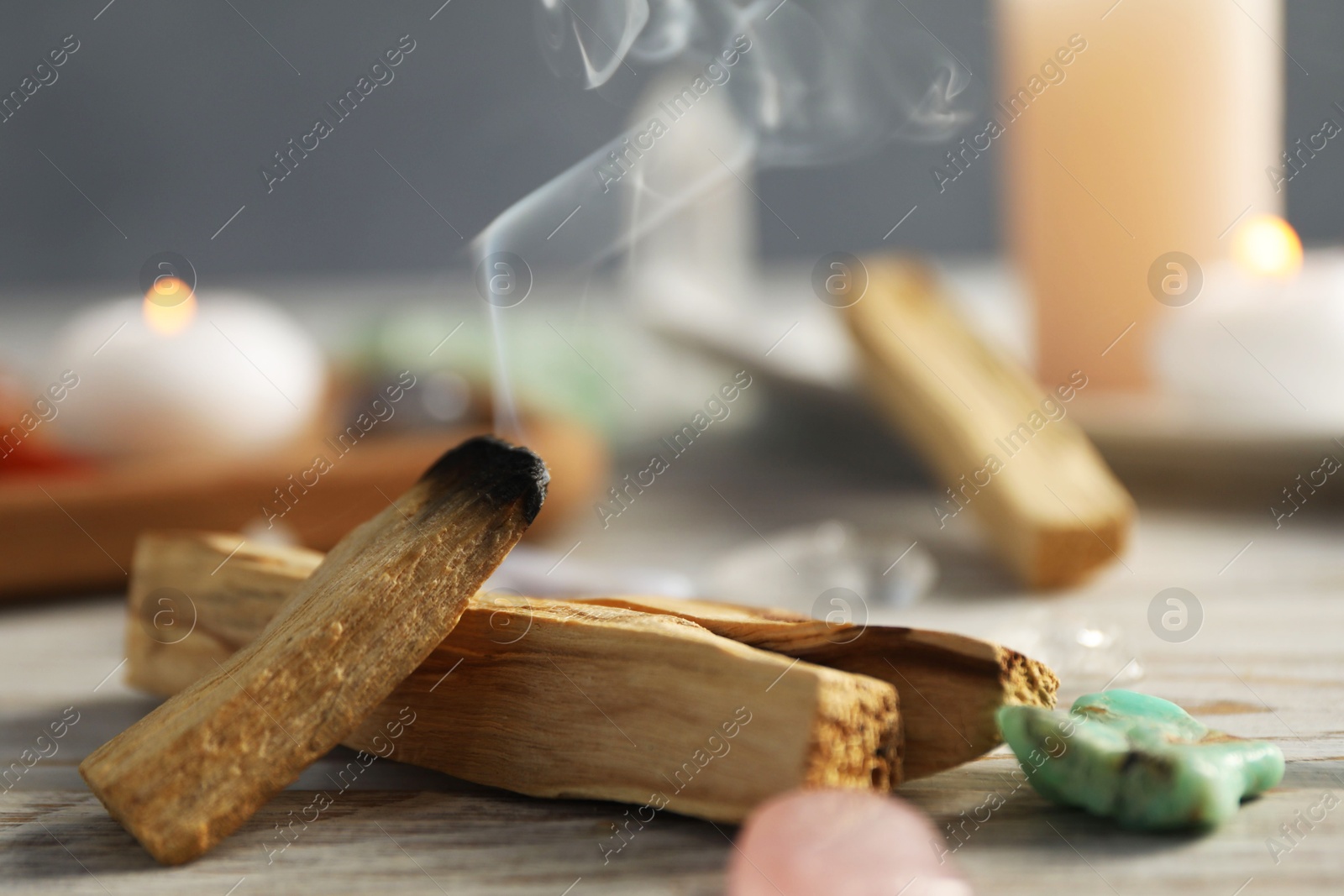 Photo of Smoldering palo santo stick and gemstones on wooden table, closeup