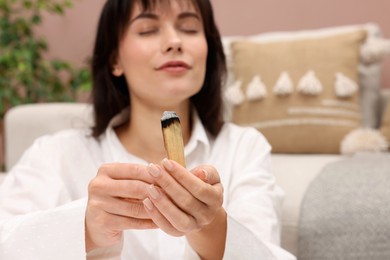 Photo of Woman with burnt palo santo stick at home, selective focus