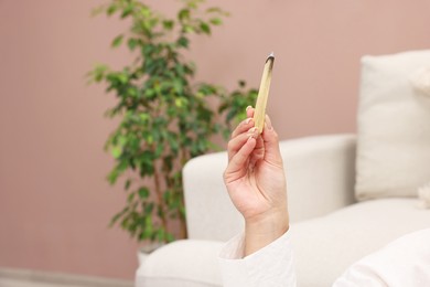 Photo of Woman with burnt palo santo stick at home, closeup. Space for text