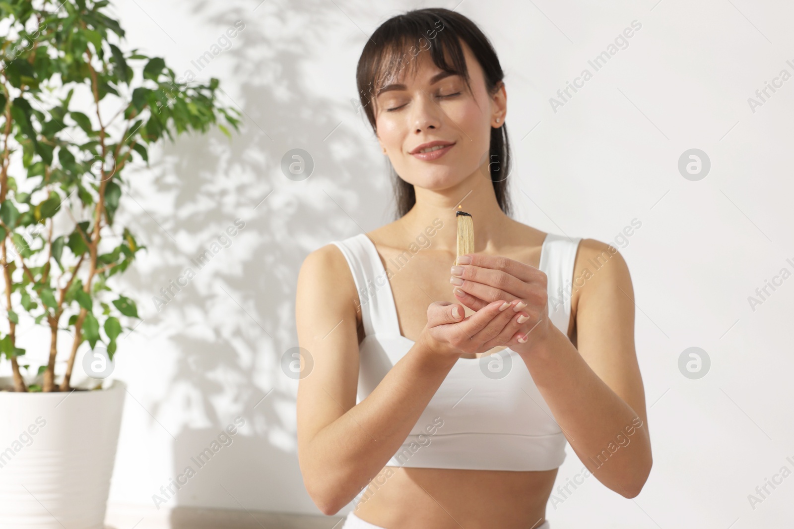 Photo of Woman with burning palo santo stick at home, space for text