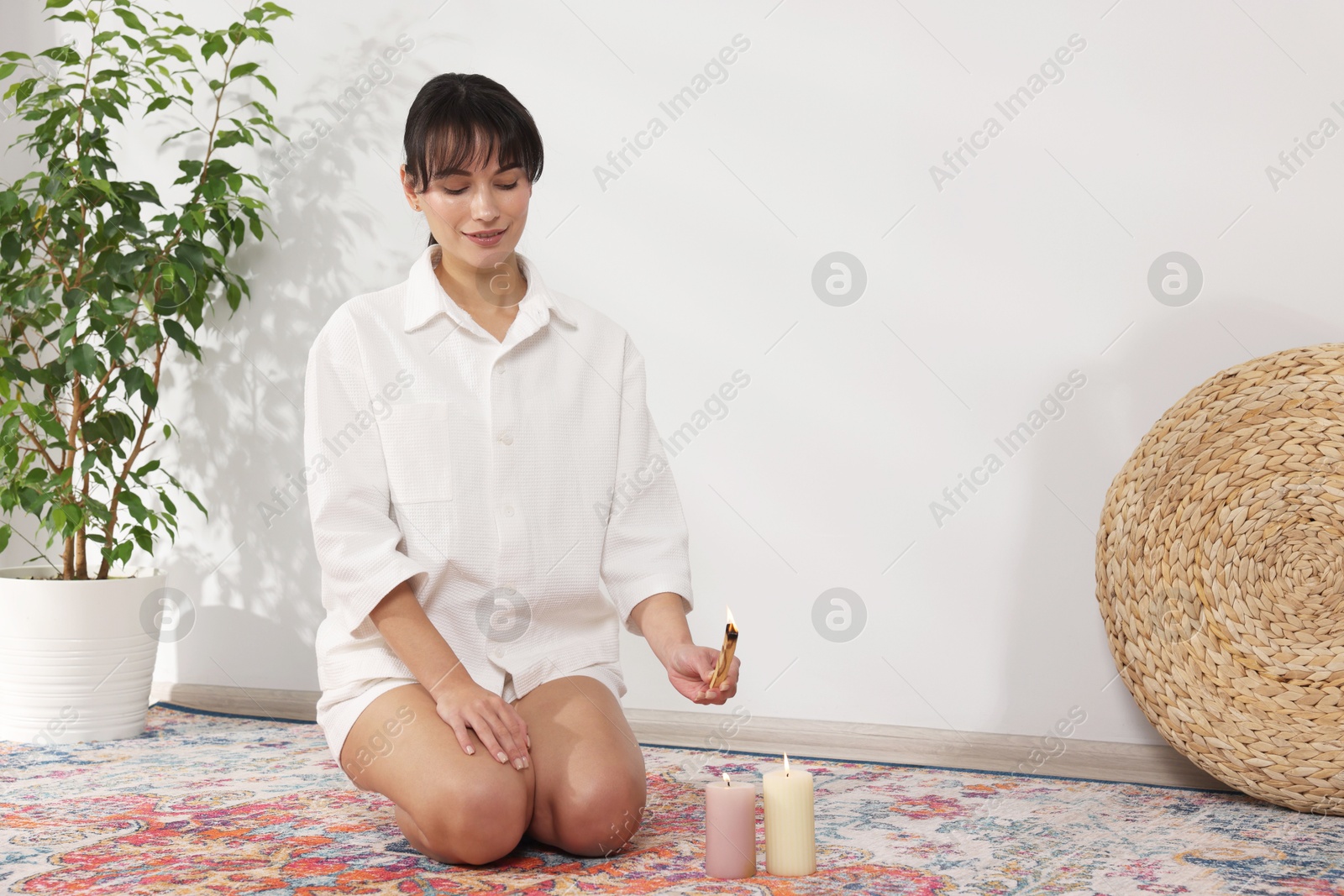 Photo of Woman with burning palo santo stick on floor at home, space for text