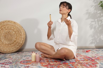 Photo of Woman with smoldering palo santo stick on floor at home