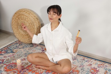 Photo of Woman with smoldering palo santo stick meditating on floor at home