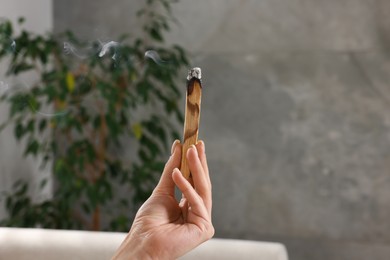 Photo of Woman with smoldering palo santo stick at home, closeup