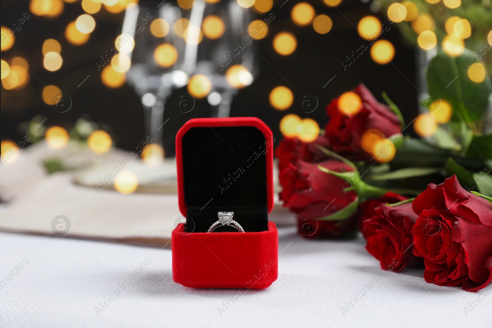 Photo of Engagement ring in box and rose flowers on white tablecloth, closeup. Romantic dinner