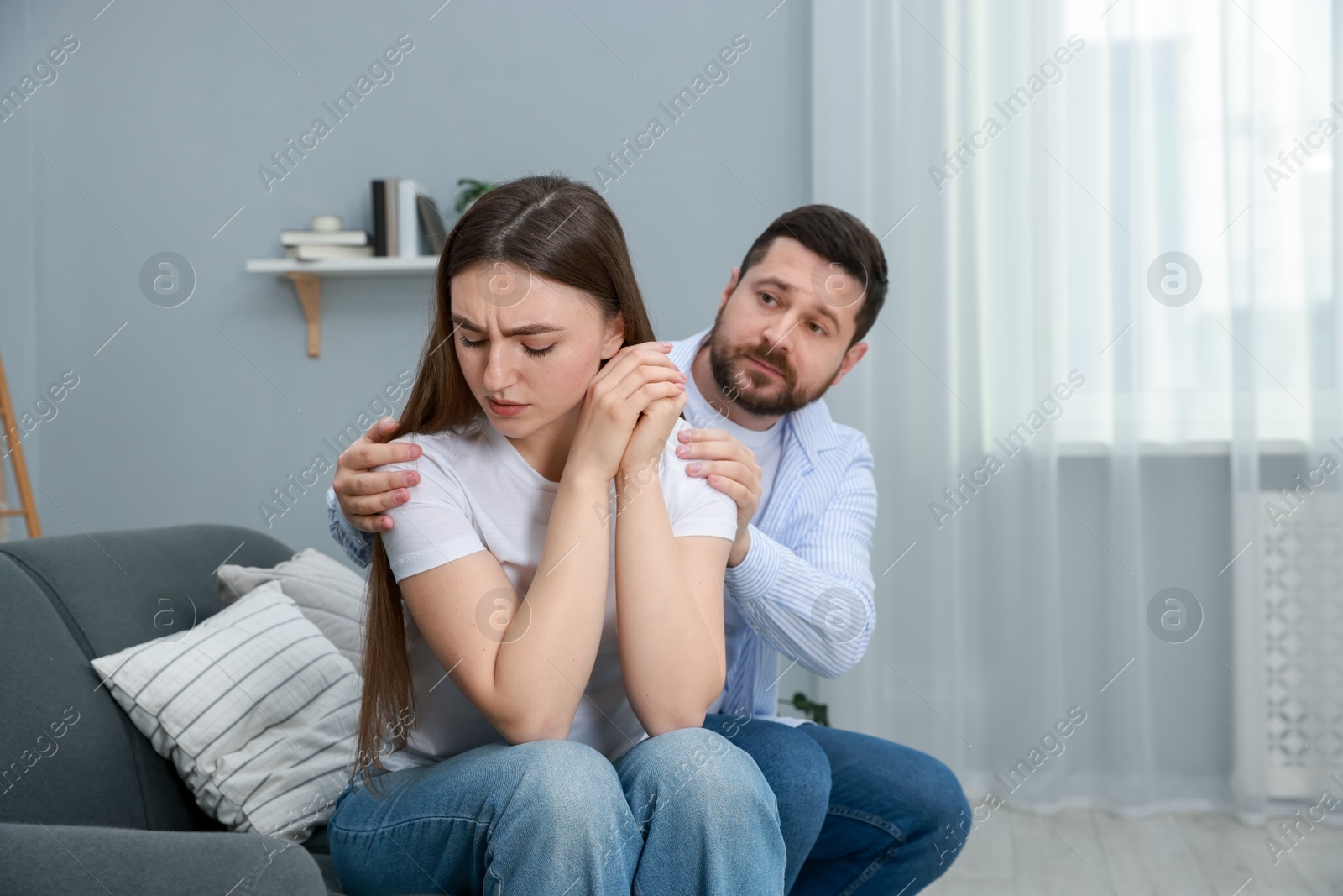 Photo of Man comforting his resentful girlfriend on couch at home, space for text