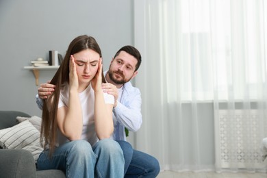 Man comforting his resentful girlfriend on couch at home, space for text