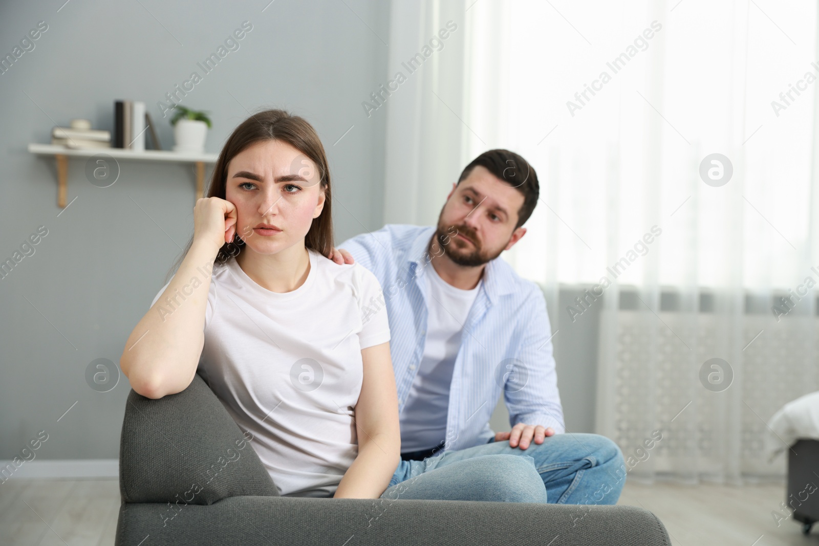 Photo of Man comforting his resentful girlfriend on couch at home, selective focus