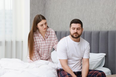 Photo of Young woman comforting her resentful boyfriend on bed at home