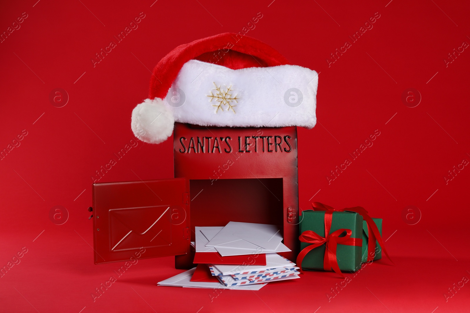 Photo of Open Santa Claus mailbox with letters, gifts and hat on red background. Christmas tradition