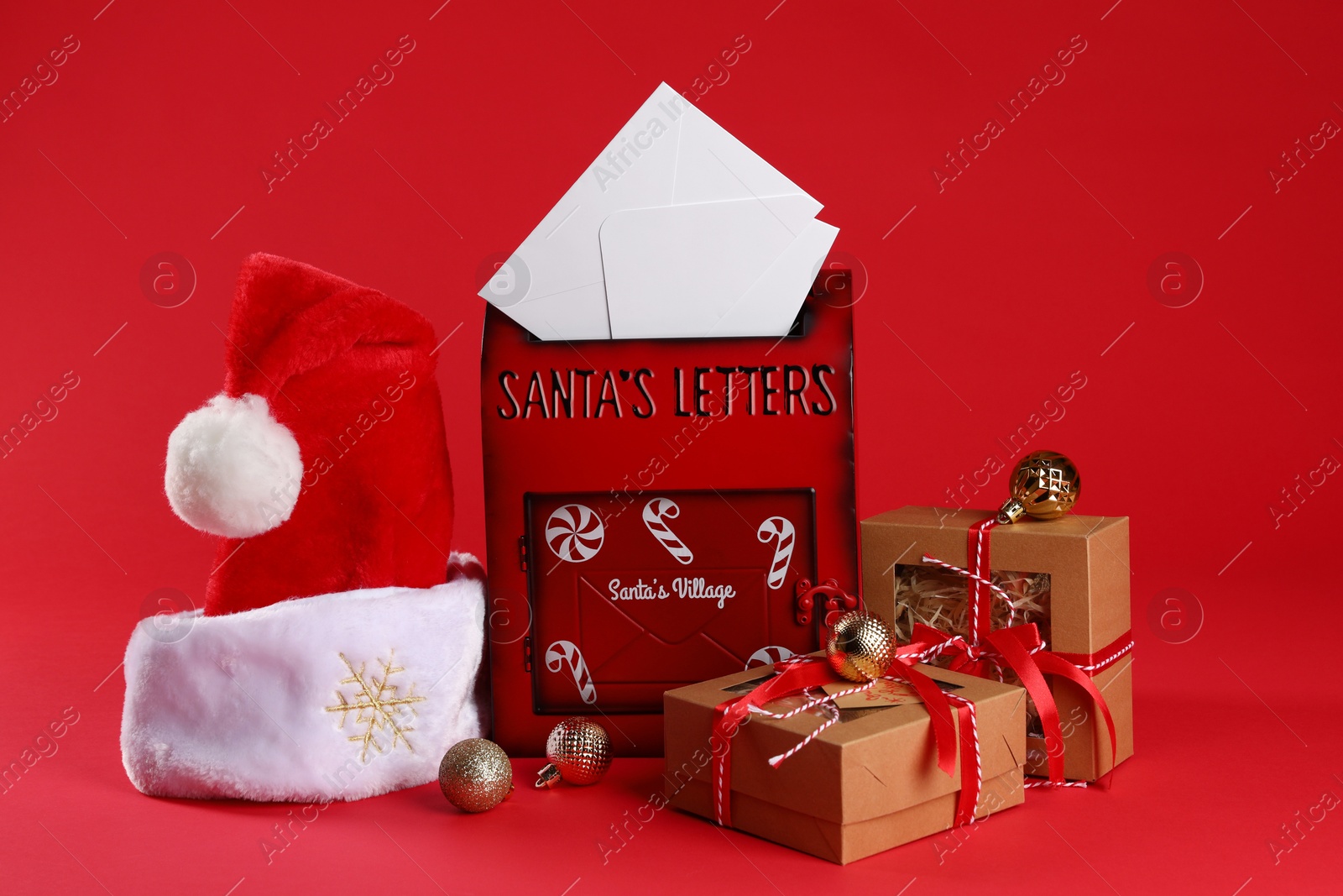 Photo of Santa Claus mailbox with letters, gifts, baubles and hat on red background. Christmas tradition