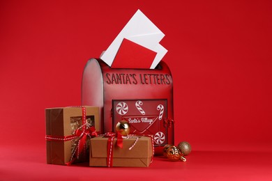 Photo of Santa Claus mailbox with letters, gifts and baubles on red background. Christmas tradition