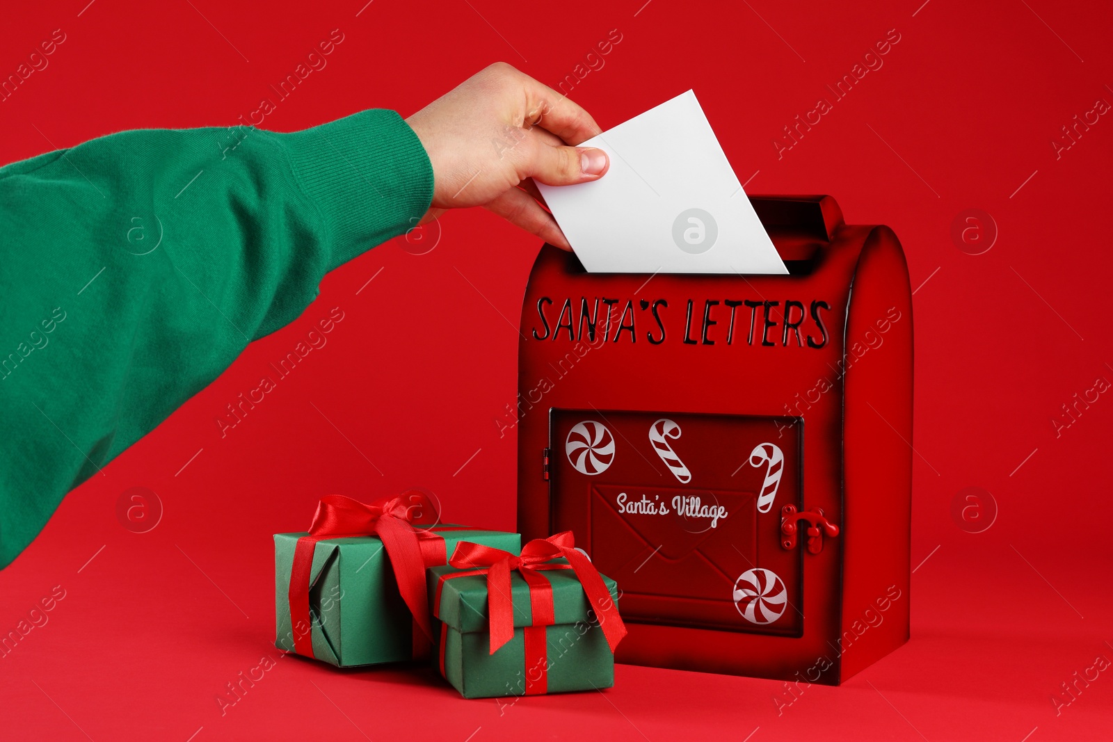 Photo of Man putting letter into Santa Claus mailbox against red background, closeup. Christmas tradition