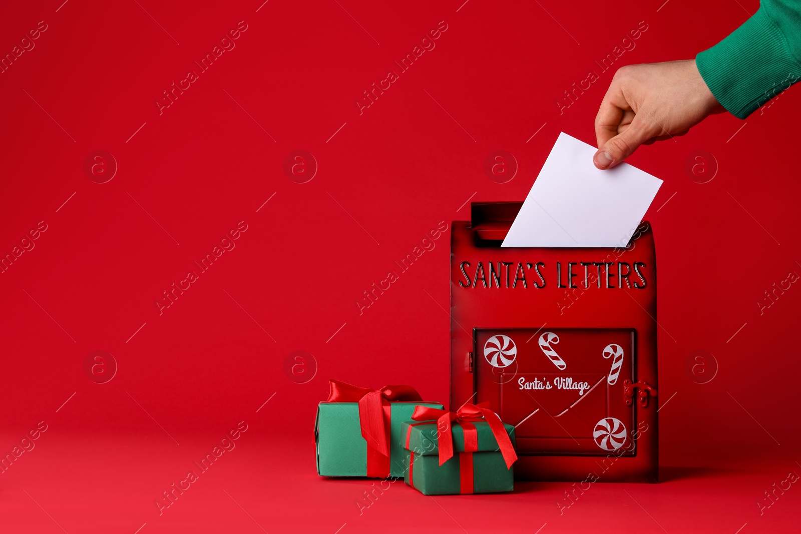 Photo of Man putting letter into Santa Claus mailbox against red background, closeup with space for text. Christmas tradition