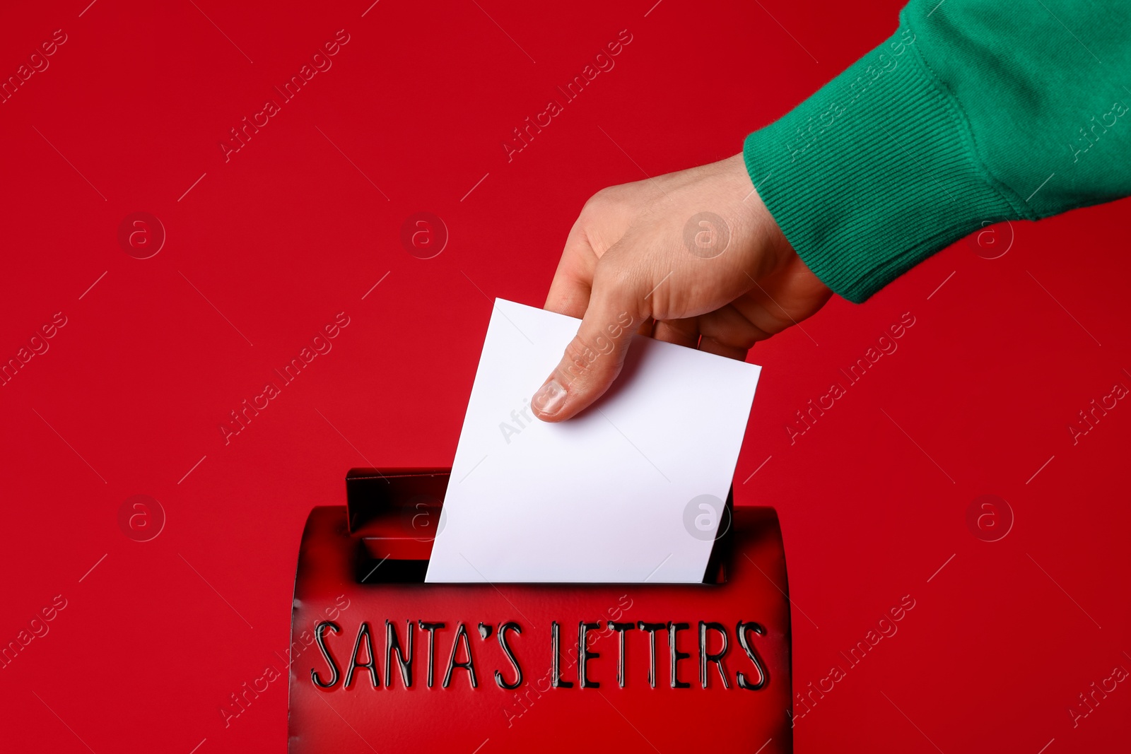 Photo of Man putting letter into Santa Claus mailbox against red background, closeup. Christmas tradition