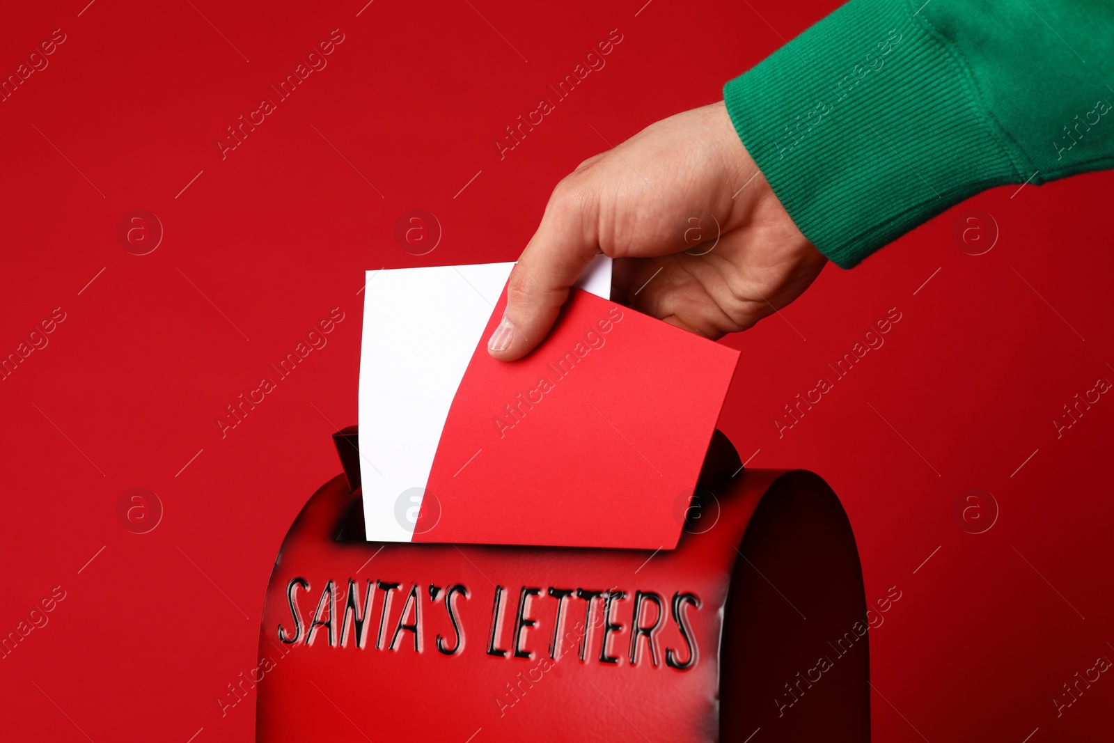 Photo of Man putting letters into Santa Claus mailbox against red background, closeup. Christmas tradition